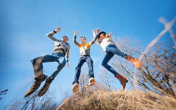 Happy cheerful smiling family jumping dancing on blue sky background in spring forest, wide angle image