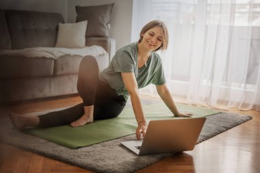 Yoga yapan çekici genç bir kadın evde yoga germe hareketleri yapıyor. Kişisel izolasyon internetteki yararlı, eğlenceli ve eğitimli bir şey. Sağlıklı yaşam tarzı kavramı