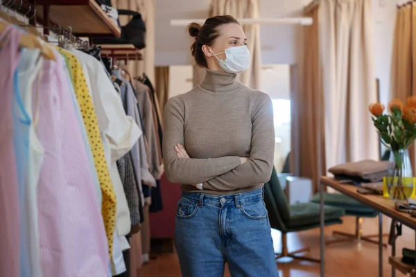 Beautiful happy young woman owner of a clothing store in a protective mask. Small business in a pandemic concept