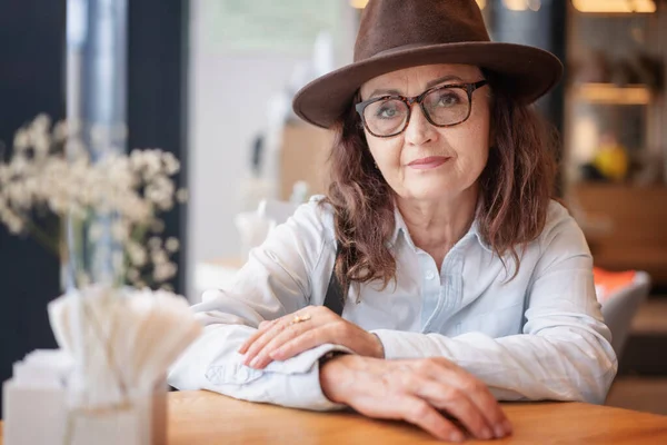 Güzel Olgun Gözlüklü Şapkalı Kafede Oturmuş Kameraya Gülümseyen Bir Kadın — Stok fotoğraf
