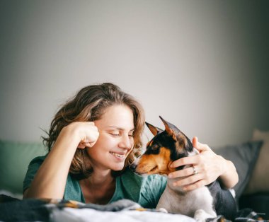 Afrika teriyeri Bassenji köpeği olan güzel, mutlu genç bir kadın. Yatakta birbirine bakıyor, portreyi yakından çekiyor.
