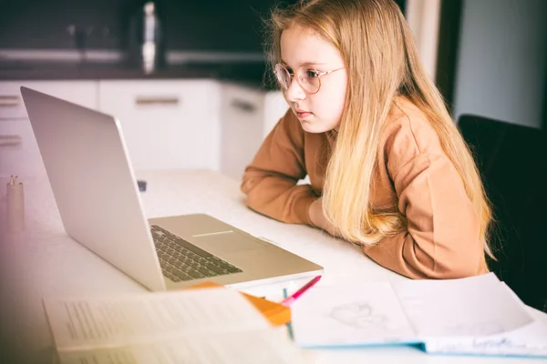 美しいです10歳ブロンド女の子で眼鏡座っています彼女の宿題をやります彼女のラップトップ — ストック写真