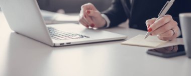 Kırmızı manikürlü kadınların elleri dizüstü bilgisayarın önündeki günlüğe not alır.