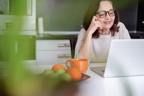 Vakava Vanhempi Nainen Laseissa Työskentelee Kotona Kannettavan Tietokoneen Kanssa Istuessaan — kuvapankkivalokuva