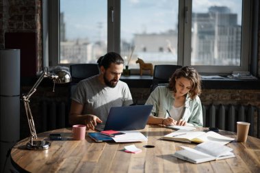 Genç insanlar hipster. Kadın ve erkek projede çalışıyor. Masada otururken dizüstü bilgisayar kullanıyorlar.