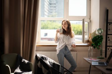 Genç, güzel esmer kadın sabah kahvesini içerken pencerenin önünde dikiliyordu.