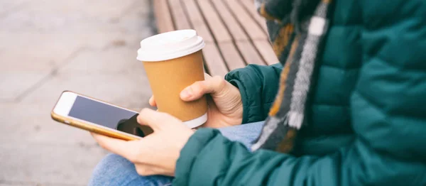 Female hands holding paper cup of takeaway coffee and smartphone, close up — Stock Photo, Image