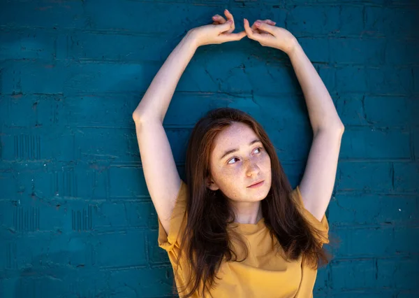 Schöne junge brünette Frau in einem gelben T-Shirt vor dem Hintergrund einer blauen Backsteinwand — Stockfoto