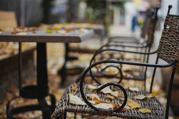 Stühle und Tische im leeren Café mit gelben trockenen Herbstblättern bedeckt — Stockfoto