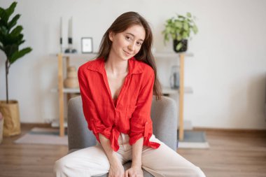 Evdeki bir sandalyede oturan kırmızı gömlekli mutlu esmer bir kadının portresi.