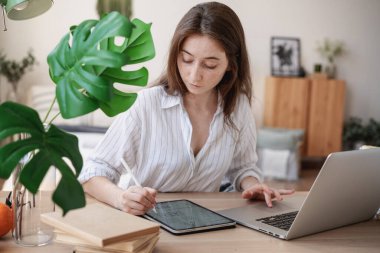 Dijital tablet ve dizüstü bilgisayarı olan genç ve güzel bir bayan öğrenci evde çalışıyor.