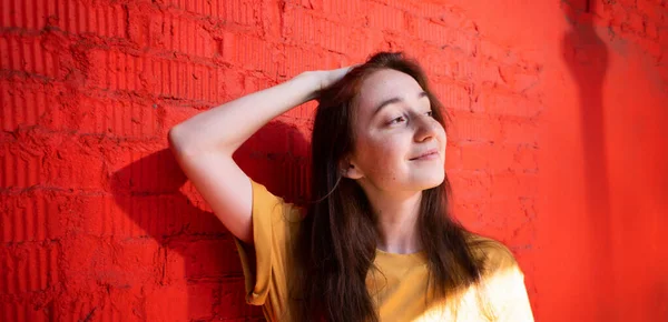 美しい若いです幸せなブルネットの女性で笑顔で黄色のTシャツ赤い壁の背景に — ストック写真