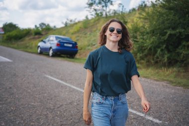 Genç ve mutlu kadın sürücü arabasının yanında dinleniyor. Yaz manzarasının tadını çıkarıyor..