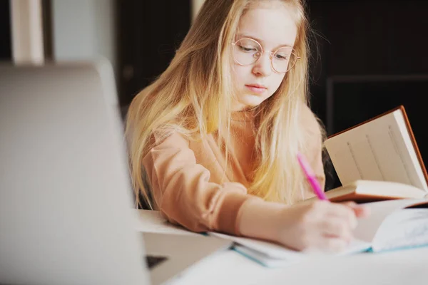 Retrato de una joven haciendo su trabajo escolar con un ordenador portátil escribiendo con un bolígrafo en un cuaderno —  Fotos de Stock