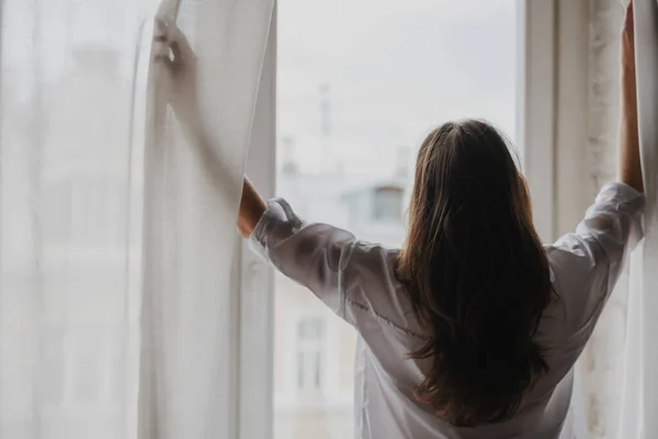 Kobieta Stojąca Przy Oknie Sypialni Otwierające Się Zasłony Widokiem Miasto — Zdjęcie stockowe