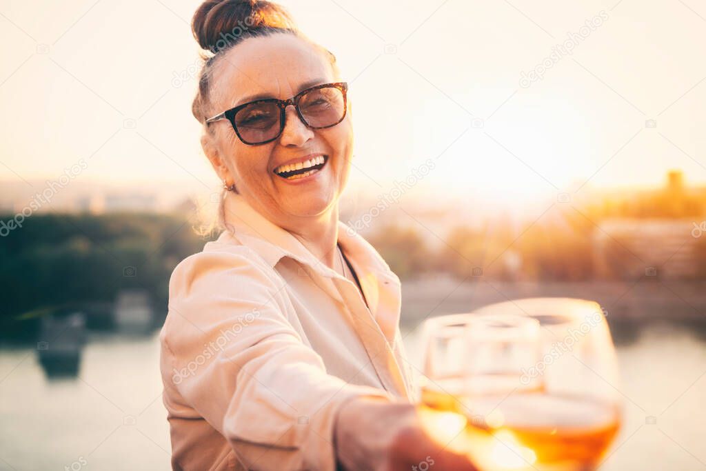 Beautiful happy mature woman enjoying a glass of wine at sunset. Active retirees lifestyle