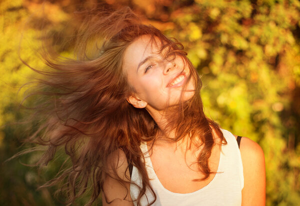 Beautiful smiling woman in a field at sunset with flying hair 