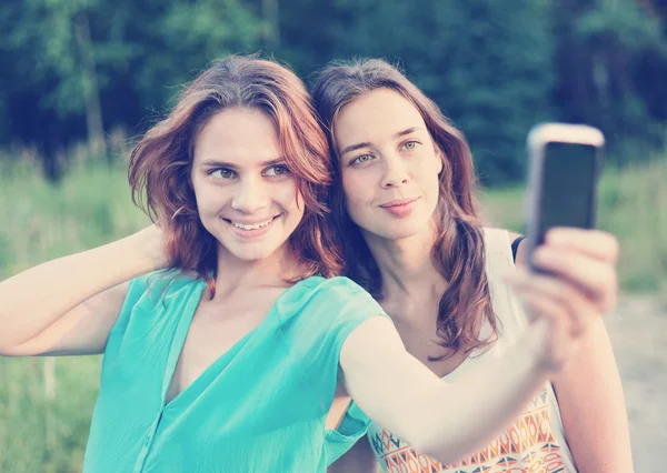 Two beautiful girls make selfie on a mobile phone — Stock Photo, Image