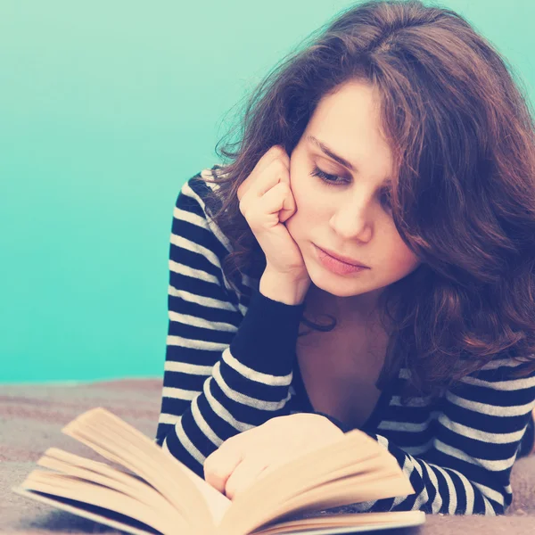 Mujer joven leyendo un libro mintiendo, en suave enfoque — Foto de Stock