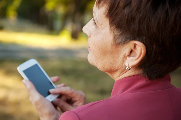 Задумчивая привлекательная женщина 50 лет с мобильным телефоном в руке — стоковое фото