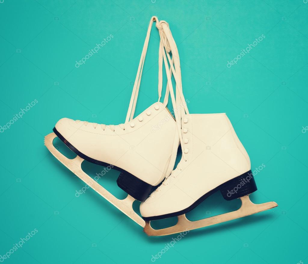 White ice skates for figure skating, hanging on a blue backgroun
