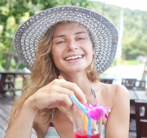Улыбающаяся молодая женщина в шляпе с коктейлем на груди — стоковое фото
