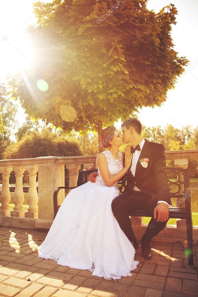 attractive bride and groom kissing, sitting on a bench