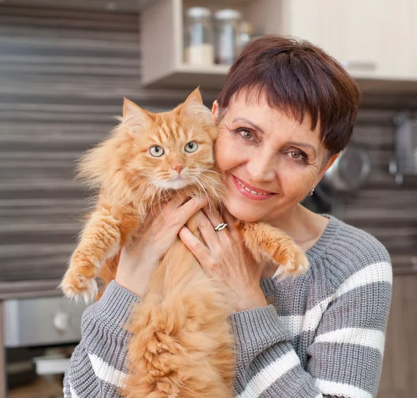 Mulher atraente de 50 anos com um gato vermelho em seus braços em casa — Fotografia de Stock