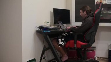 Yüksek çözünürlüklü, uzun saçlı, esneyen ve sigara içen bir erkeğin laptopuyla evden çalışırken çekilmiş görüntüleri.