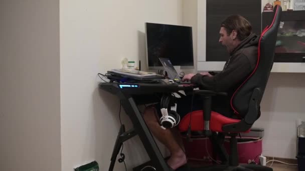 HD-кадры взрослого мужчины с длинными волосами, зевающего и курящего сигарету, работающего из дома на своем ноутбуке — стоковое видео
