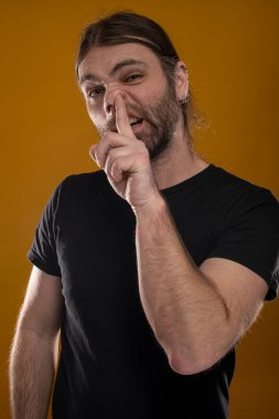 Sol kolunu burnuna sokarken yüzünü buruşturan kaba bir erkeğin portresi. Bal sarısı bir arka planda izole edilmiş.