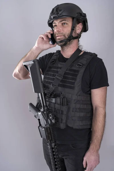 Man equipped for airsoft with helmet and protective vest is confirming the negociation strategy on the phone while standing with his weapon displayed