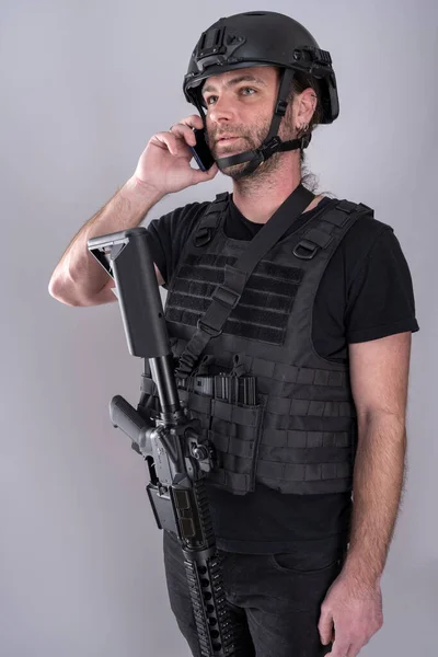 Mężczyzna wyposażony w kask i kamizelkę ochronną potwierdza strategię negocjacji przez telefon stojąc z bronią na widoku. Obrazy Stockowe bez tantiem