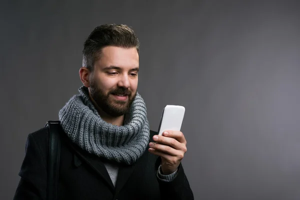 Man in winter clothes with smartphone texting, studio shot — Stock Photo, Image