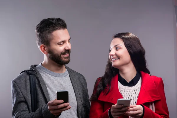 Young woman and man in winter clothes with smartphone — Stockfoto