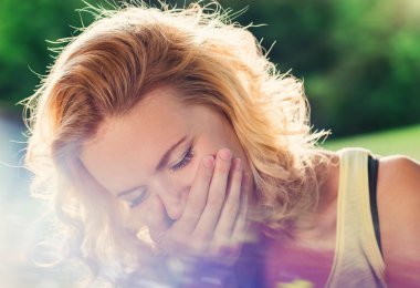 Sarışın kadın gülüyor, eliyle ağız tutuyor. Güneşli yaz