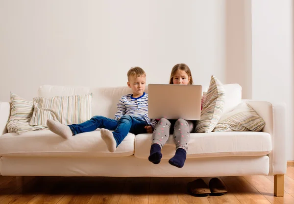 Anak-anak di rumah duduk di sofa, bermain dengan laptop — Stok Foto