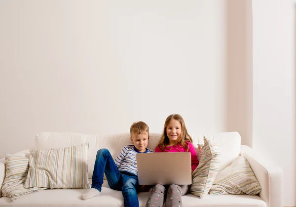 Los niños en casa sentados en el sofá, jugando con el ordenador portátil — Foto de Stock