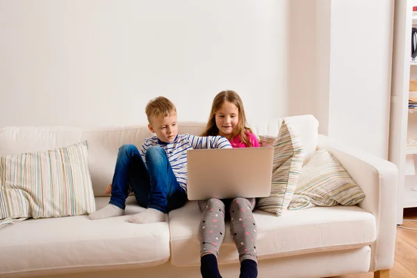 Crianças em casa sentadas no sofá, brincando com laptop — Fotografia de Stock