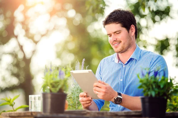 Gardener with tablet, sitting at the table, green nature — Stock Photo, Image