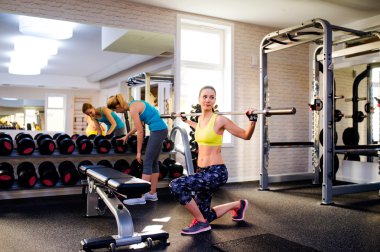 Women in gym exercising with weights and bar