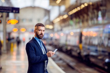 Hipster işadamı akıllı telefon, bekleyen, tren platformu ile