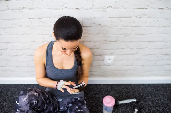 Fit woman in gym holding smart phone, brick wall — Stock Fotó