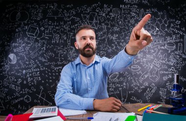 Teacher at desk, school supplies, raised finger, big blackboard