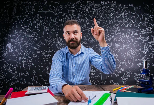 Lehrer am Schreibtisch, Schulmaterial, erhobener Finger, große Tafel — Stockfoto