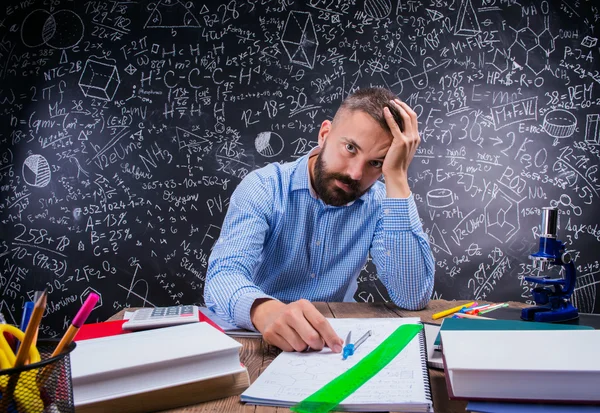 Insegnante sconvolto alla scrivania, materiale scolastico, testa in mano, lavagna — Foto Stock