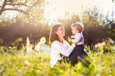 Mother holding her little son, sitting on the grass