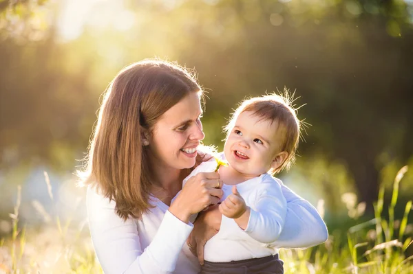 Mother holding her little son, sitting on the grass