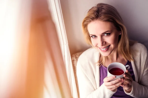 Woman on window sill with cup of tea
