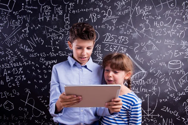 Boy and girl with tablet at blackboard — Stock Photo, Image